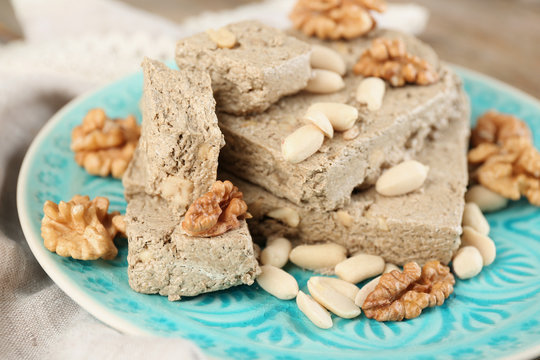 Sunflower halva with nuts on plate, on wooden background