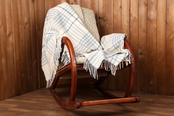 Fototapeta na wymiar Rocking chair covered with plaid on wooden wall background
