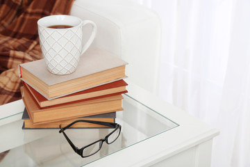 Tabletop with pile of books, cup and glasses near the sofa
