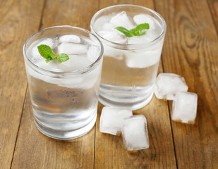 Glass of water with ice cubes on wooden table