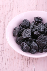 Bowl of prunes on color wooden background