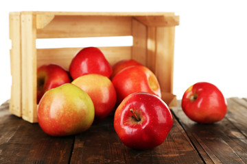 Spilled red apples near crate on wooden table isolated on white