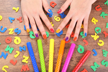 Multicolor female manicure with markers on wooden background