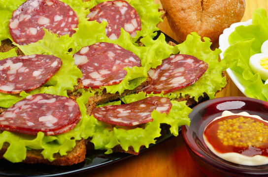 Sliced sausage on a black plate and quail eggs on lettuce leaves