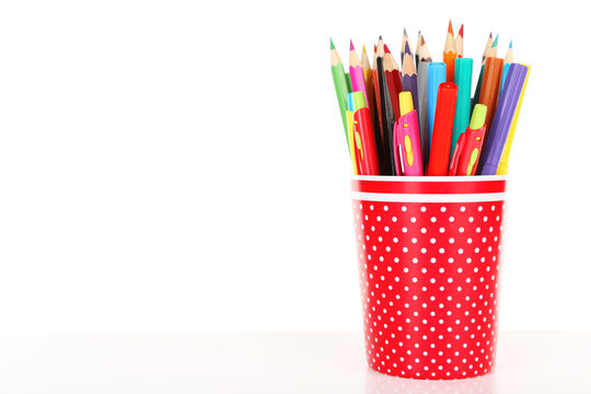 Colorful pens, pencils and markers in red polka-dot plastic cup