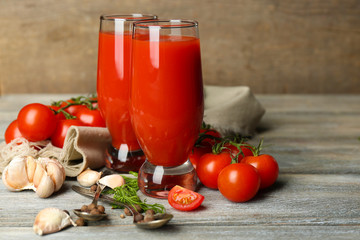 Glasses of tasty tomato juice and fresh tomatoes on wooden