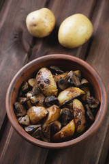 Ceramic bowl with roasted potato slices and mushrooms, close-up