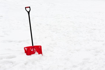 Red plastic shovel with black handle stuck in fluffy snow.