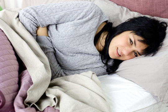 Woman with strong menstruation stomach ache lying in bed