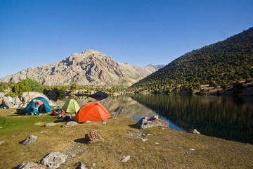 blue mountain lake reflects high rocks with camp near it