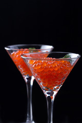 Red caviar in wineglasses on black background