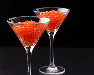 Red caviar in wineglasses on black background