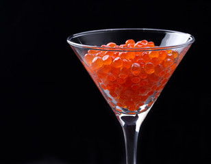 Red caviar in wineglass on black background