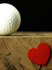 Golf ball and heart on the edge of table.