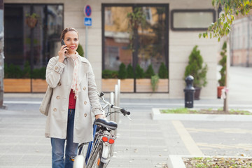 Fototapeta na wymiar Young woman holding a bicycle talking on the phone on the street