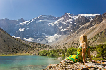 girl sitting on a bank of blue mountain lake