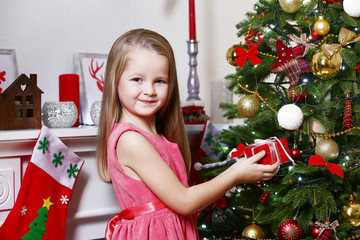 Little girl holding present box near fir tree