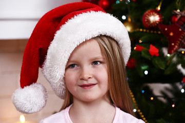 Little girl in Santa hat near fir tree on fireplace background