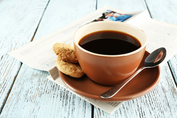 Cup of coffee with newspaper on color wooden background