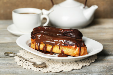 Tasty eclairs and cup of tea on wooden table