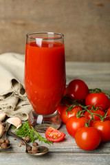 Glass of tasty tomato juice and fresh tomatoes on wooden table