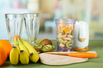 Sliced fruits and blender on wooden table, on bright background