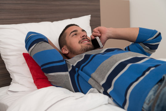Happy Young Man Using Phone On Bed