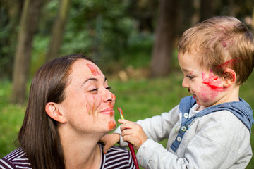 Happy child painting his mother´s face in the park