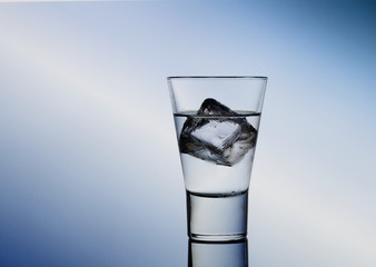 Short drink glass with clear liquid and ice cubes