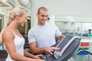 Fototapeta na wymiar Trainer assisting woman with treadmill screen options at gym