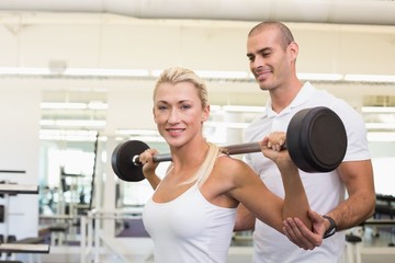 Fototapeta na wymiar Trainer helping woman with lifting barbell in gym