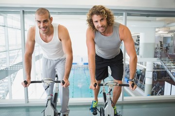 Fit men working on exercise bikes at gym
