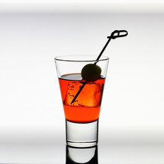Short drink glass with red liquid, olive, ice cubes