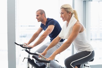 Fototapeta na wymiar Determined couple working on exercise bikes at gym