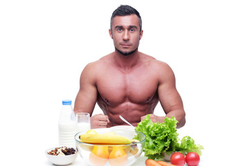 Happy muscular man sitting at the table with healthy food