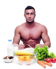 Muscular sports man sitting at the table with healthy food