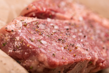 Raw beef steak seasoned with salt and pepper on a dark paper 