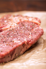 Raw beef steak seasoned with salt and pepper on a dark paper 