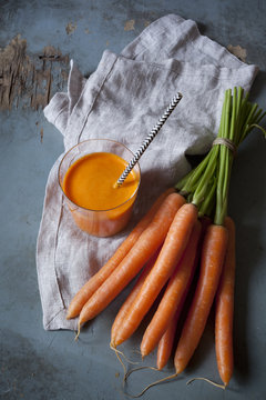 carrot smoothie on glass with straw and carrots bunch
