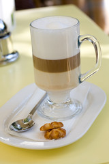Latte in a transparent glass and two cookies on a white plate