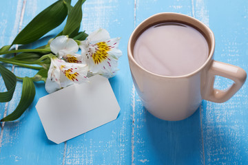 Alstroemeria flower, cup of coffee and blank card on the table