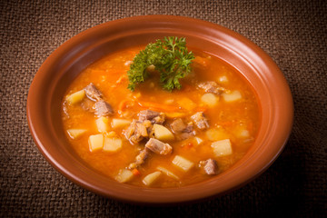 Ceramic plate of vegetable soup standing on sackcloth. tinted