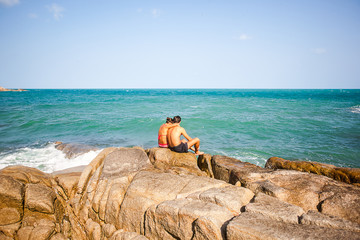 Fototapeta na wymiar young couple sitting on the rocks near shore and hug