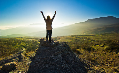 girl with hands up in the mountsins against sun