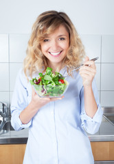 Lachende Frau mit blonden Locken in der Küche liebt Salat