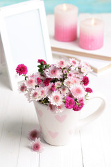 Beautiful flowers in cup on table on light blue background