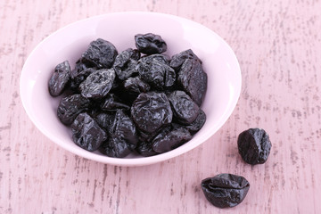Bowl of prunes on color wooden background