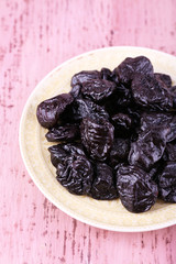 Plate with heap of prunes on color wooden background