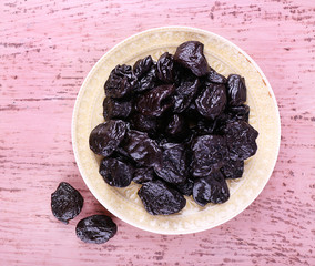 Plate with heap of prunes on color wooden background
