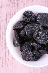 Bowl with heap of prunes on color wooden background